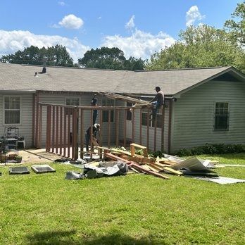 A group of people are working on a porch in front of a house.