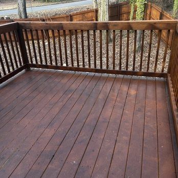 A wooden deck with a railing and a fence in the background.