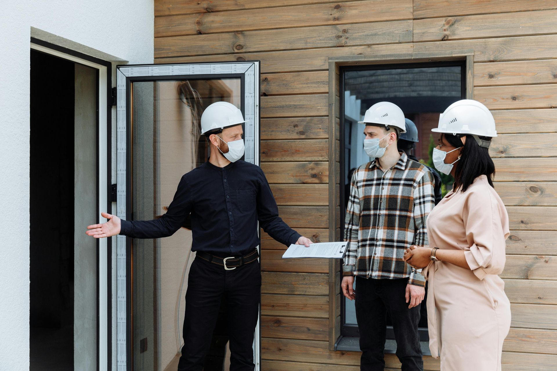 A group of people wearing hard hats and masks are standing in front of a building.
