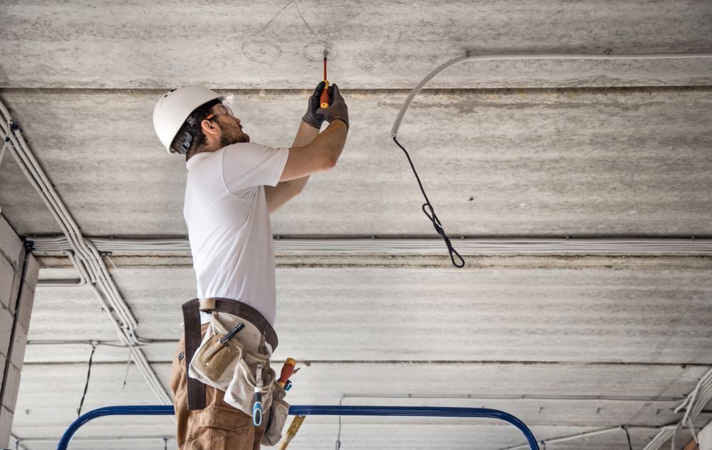 A Man Is Standing On A Ladder Working On An Electrical Wire In The Ceiling — Barcou Electrics In Gordonvale, QLD