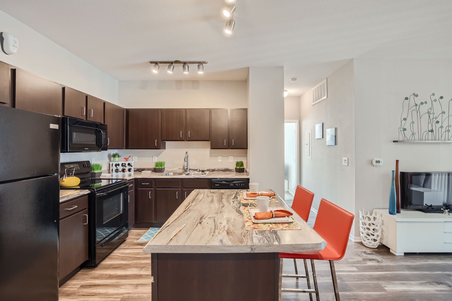 Open-concept kitchen with dark wood cabinets, granite countertops, and orange bar stools.