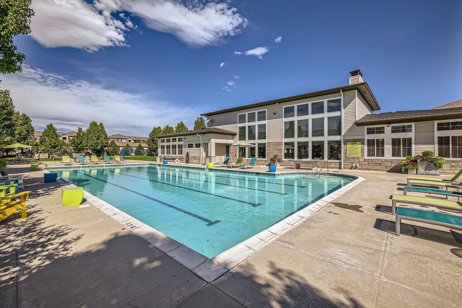 Outdoor apartment community pool with colorful lounge chairs and a modern clubhouse.