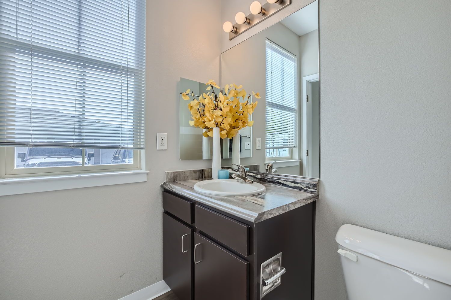 Bathroom vanity with marble-look countertop, single sink, dark cabinets, and window blinds.