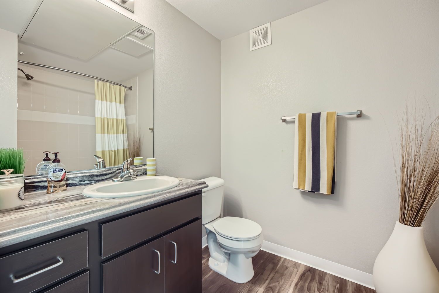 Bathroom with dark wood vanity, mirror, toilet, striped towel, and shower curtain.