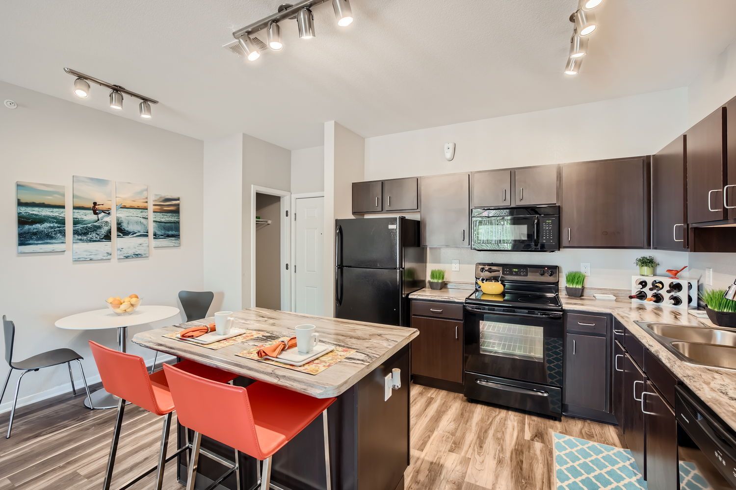 Open-concept apartment kitchen with dark cabinetry, black appliances, and a central island with red stools.