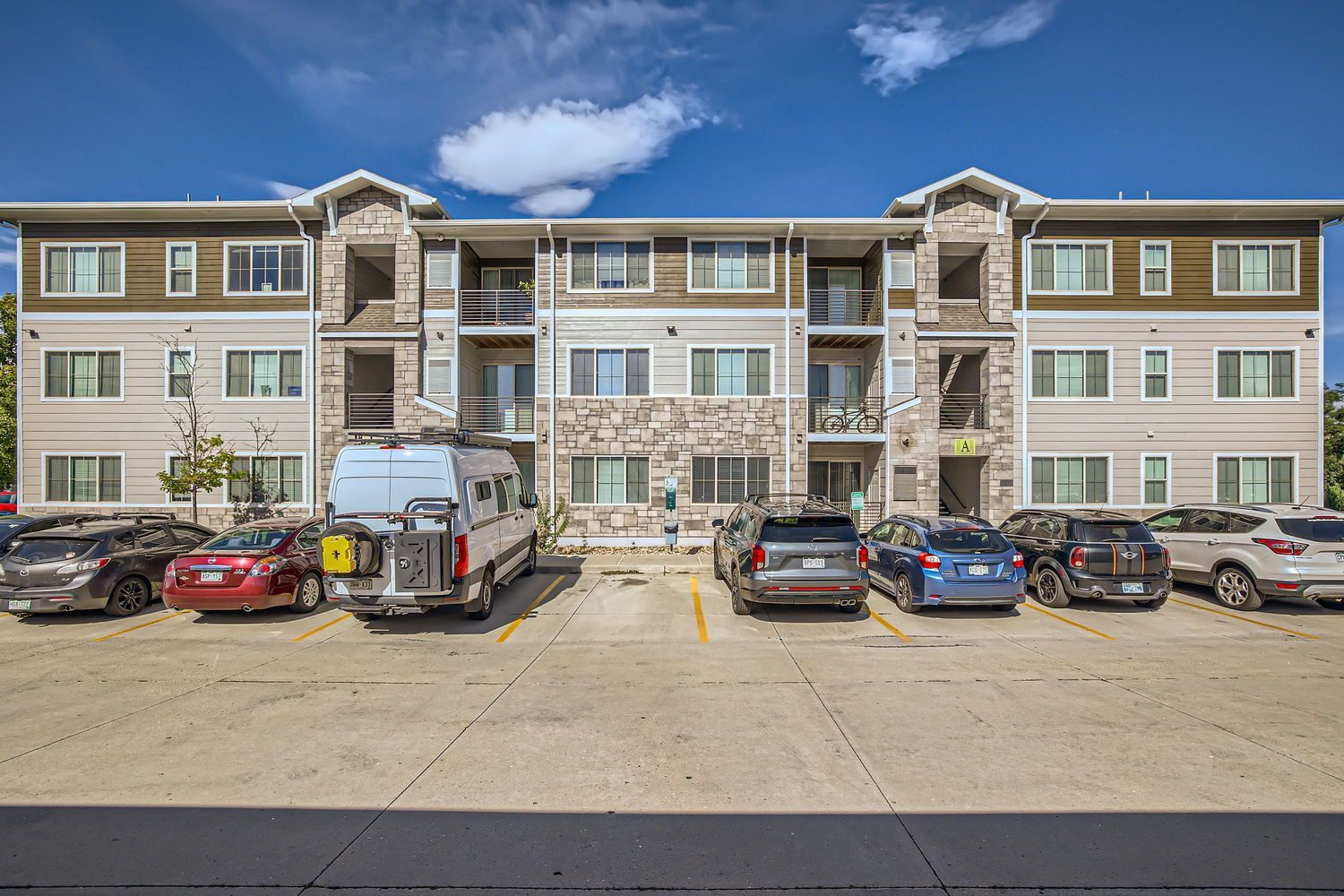 Exterior view of a modern, multi-story apartment building with a front parking lot.