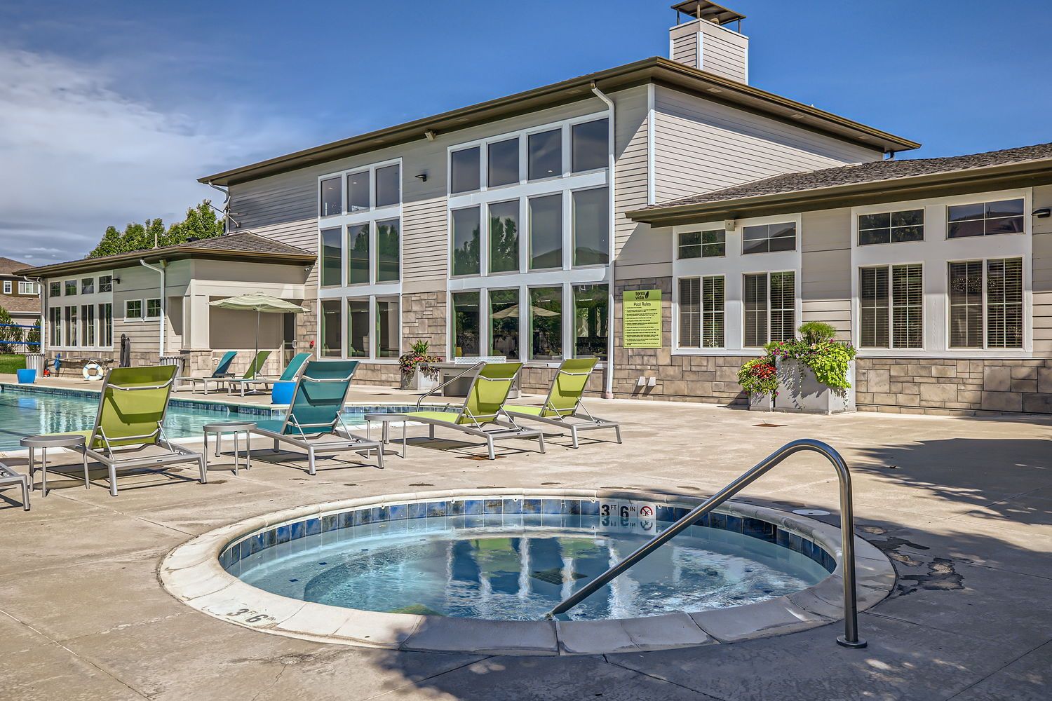 Outdoor apartment community pool area with lounge chairs and a glass-front building.