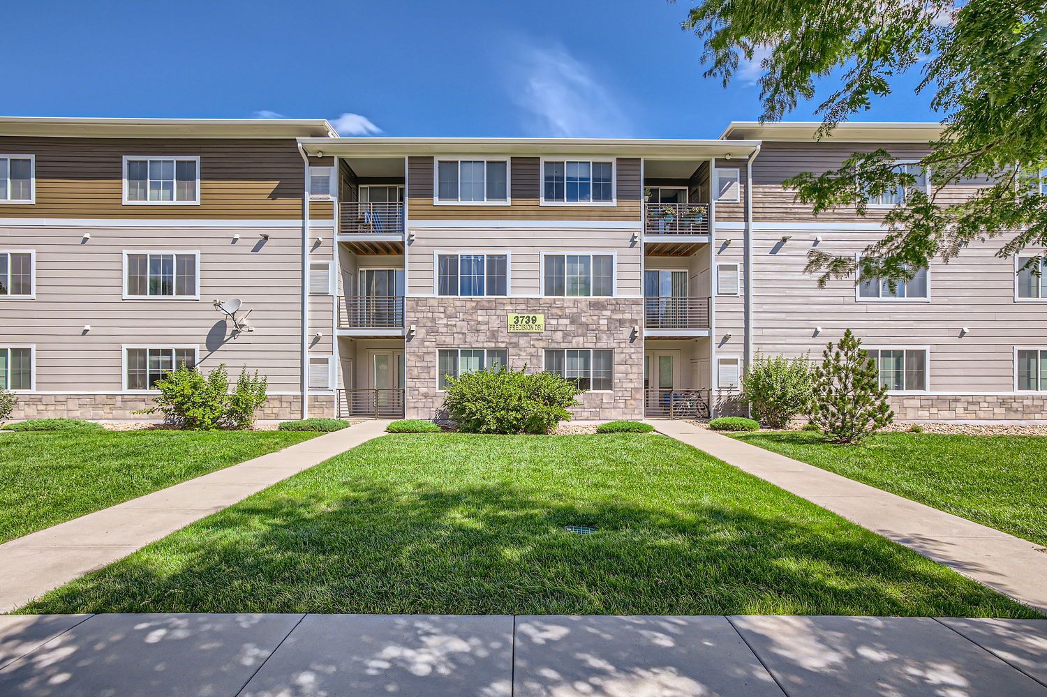 Front exterior view of a modern apartment building with a green lawn and walkways.