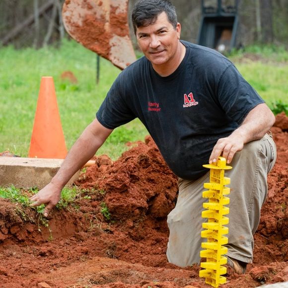 A man in a black shirt is kneeling in the dirt holding a yellow object