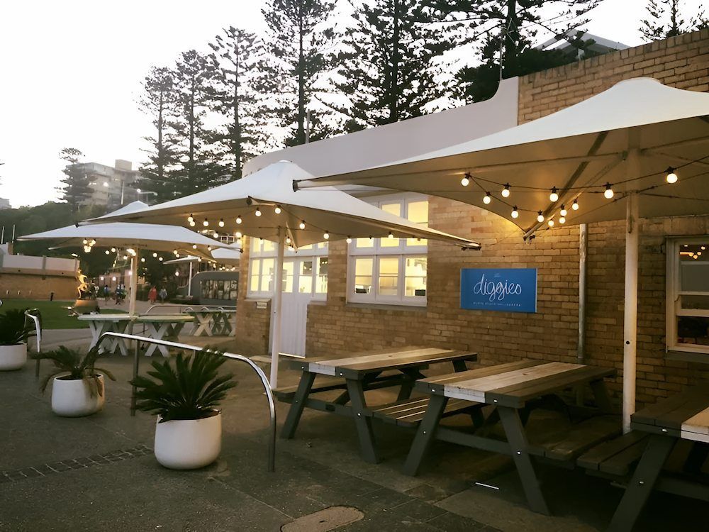 A Brick Building With Picnic Tables and Umbrellas in Front of It — Mylec Electrical Solutions in Shellharbour, NSW