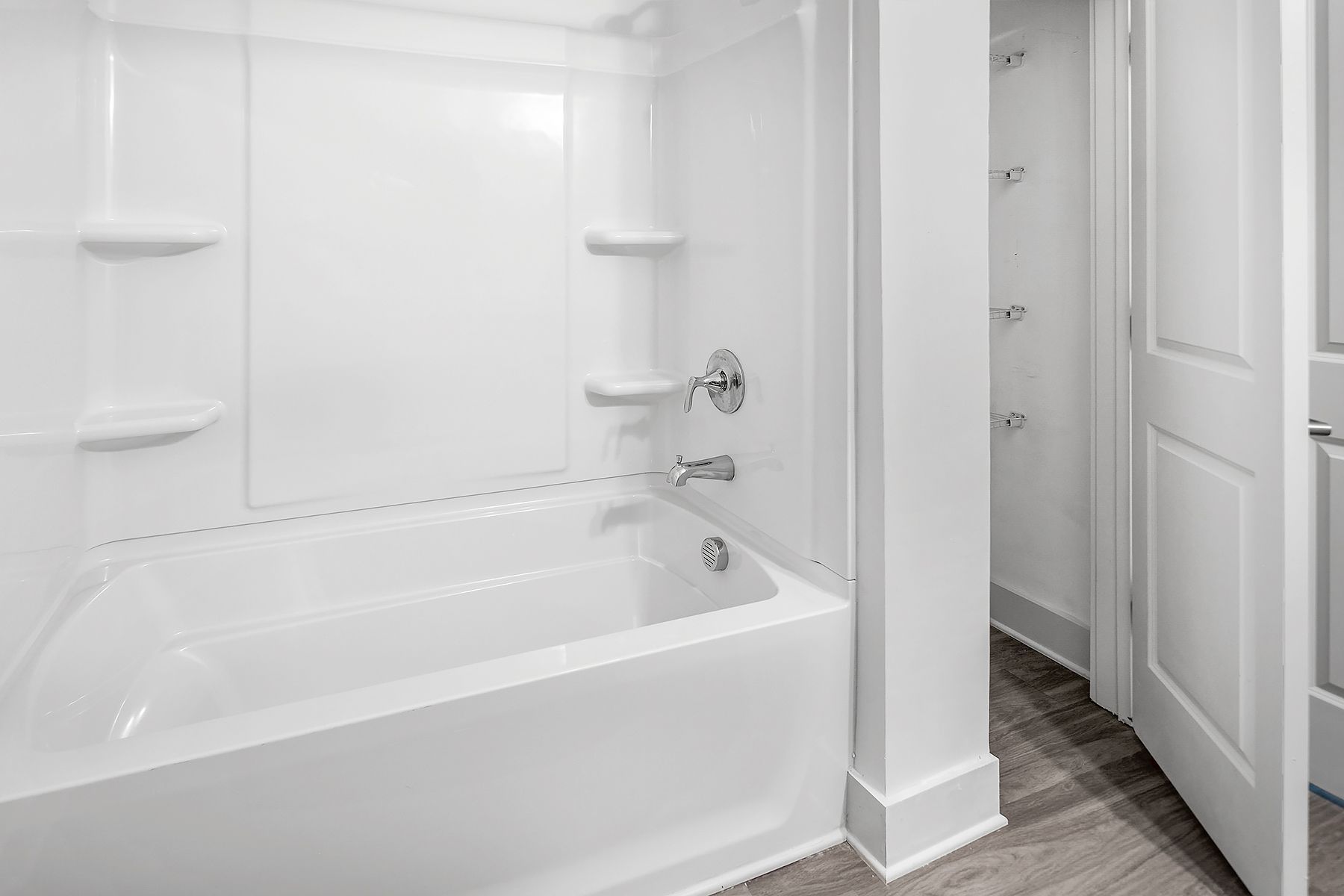 White bathroom with tub and shelving; doorway on the right.