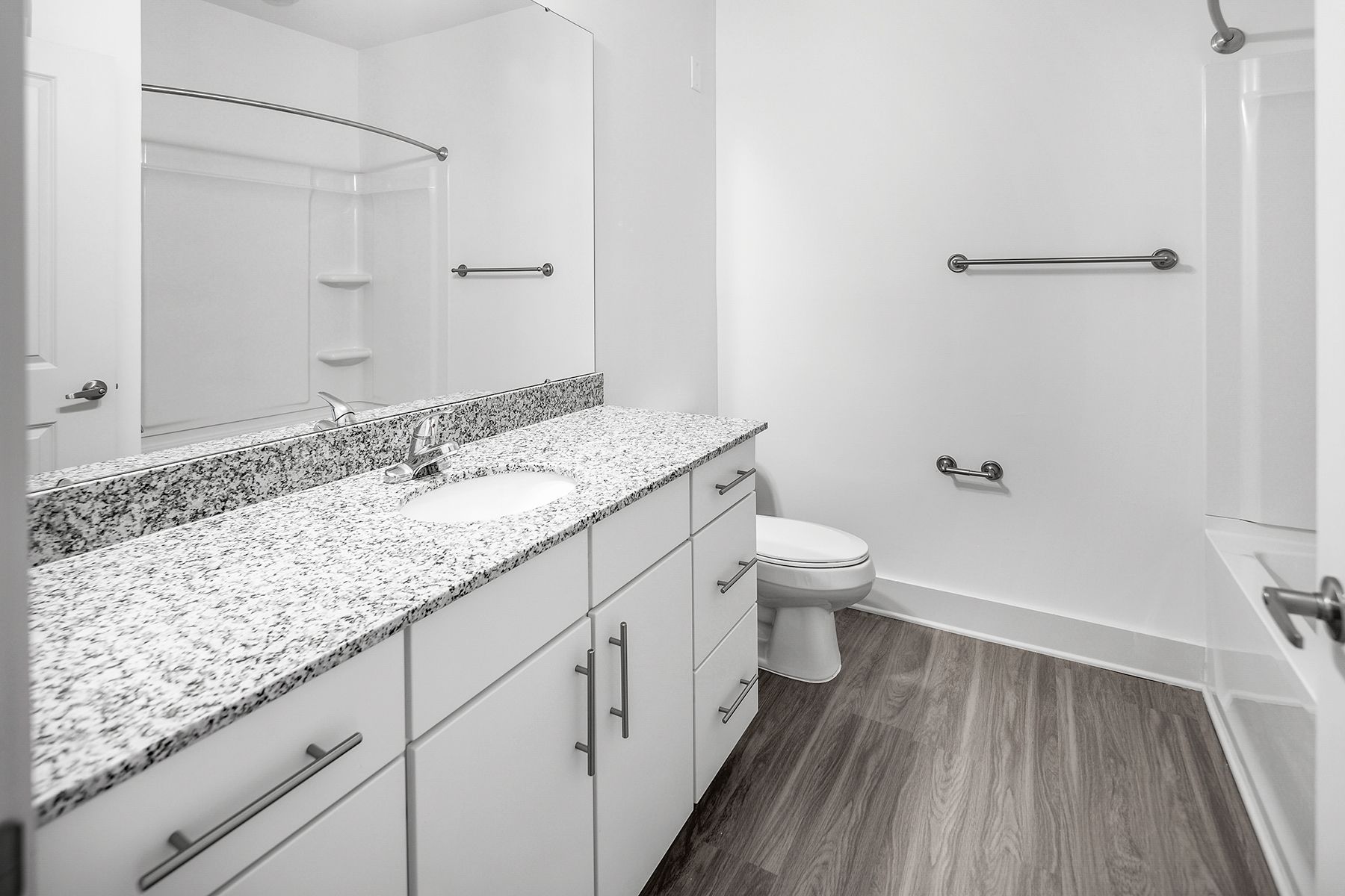 Bathroom with a white vanity, granite countertop, toilet, and shower. Gray wood-look flooring.