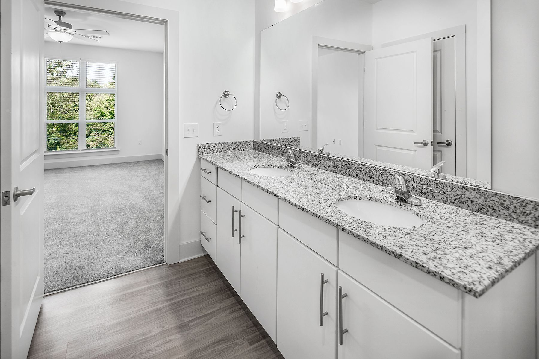 Bathroom with white cabinets, granite countertop, and doorway leading to a bedroom.