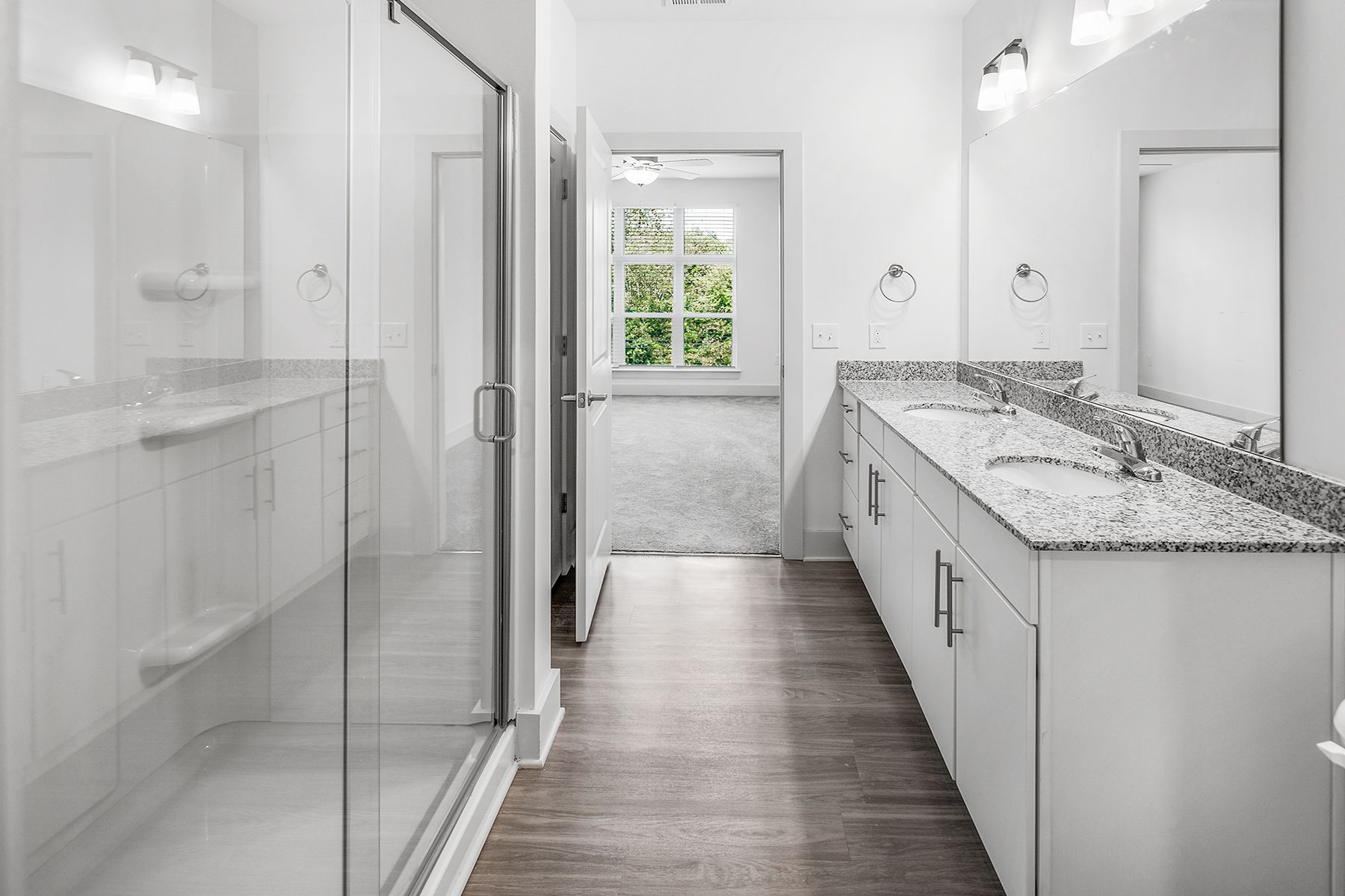Modern white bathroom with double sinks, glass shower, and wooden floors.
