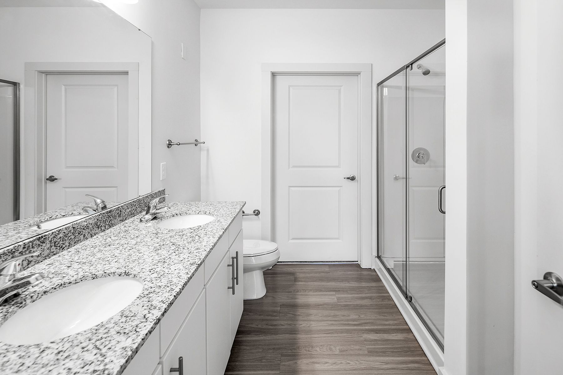Bathroom with double vanity, granite countertop, toilet, and glass shower.