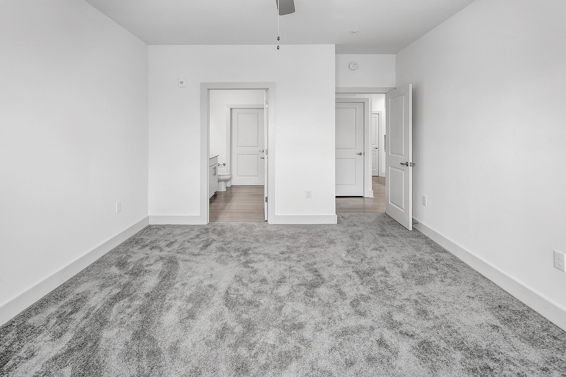 Empty room with gray carpet and white walls, with doorways leading to other rooms.