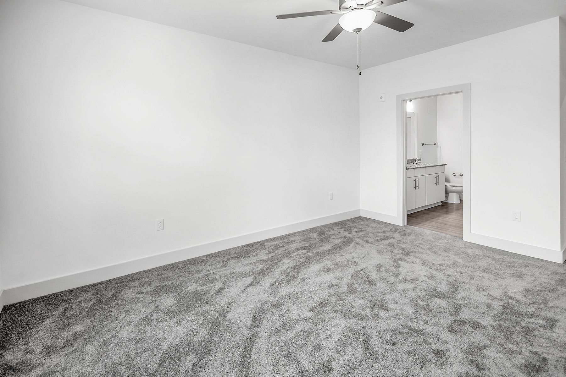 Empty bedroom with gray carpet, white walls, and a doorway to a bathroom.