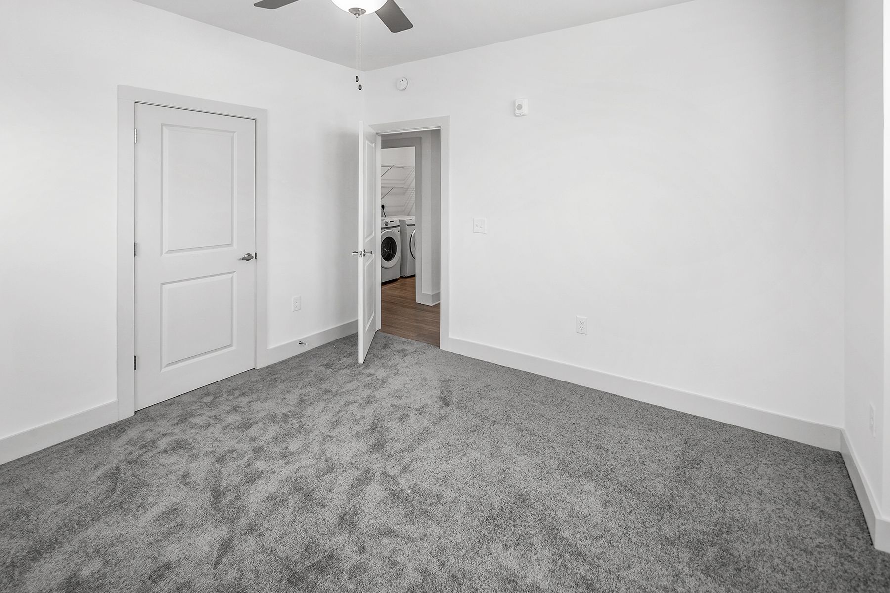 Empty bedroom with gray carpet, white walls, and open door to a laundry room.