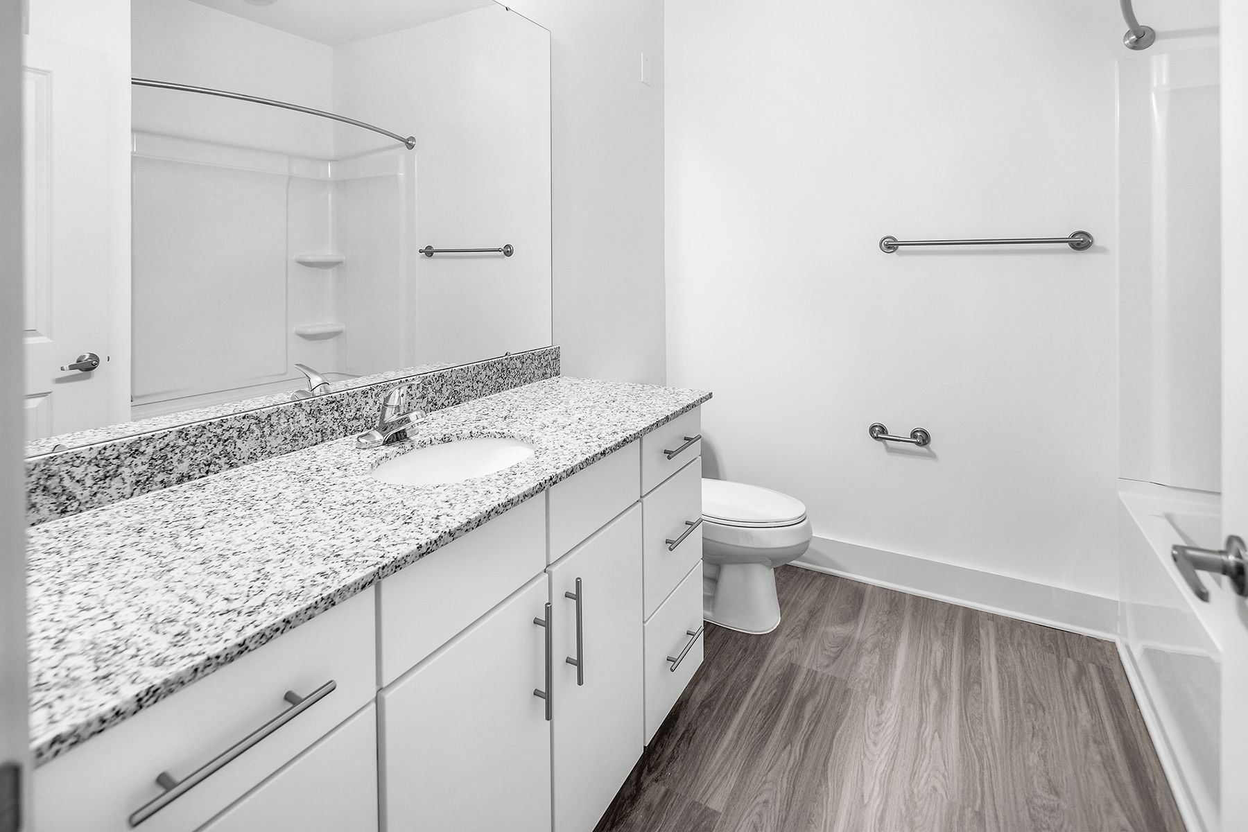Bathroom with white cabinets, granite countertop, toilet, and shower; gray wood-look flooring.