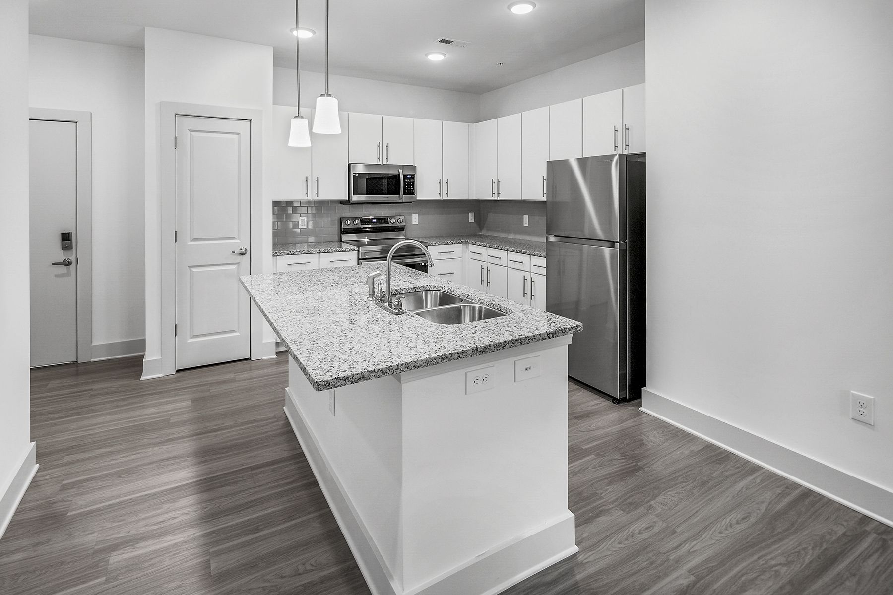 Modern kitchen with white cabinets, granite island, stainless steel appliances, and wood flooring.