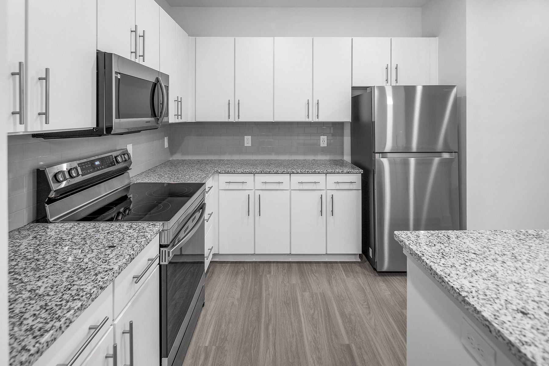 Modern white kitchen with stainless steel appliances, granite countertops, and light wood-look flooring.