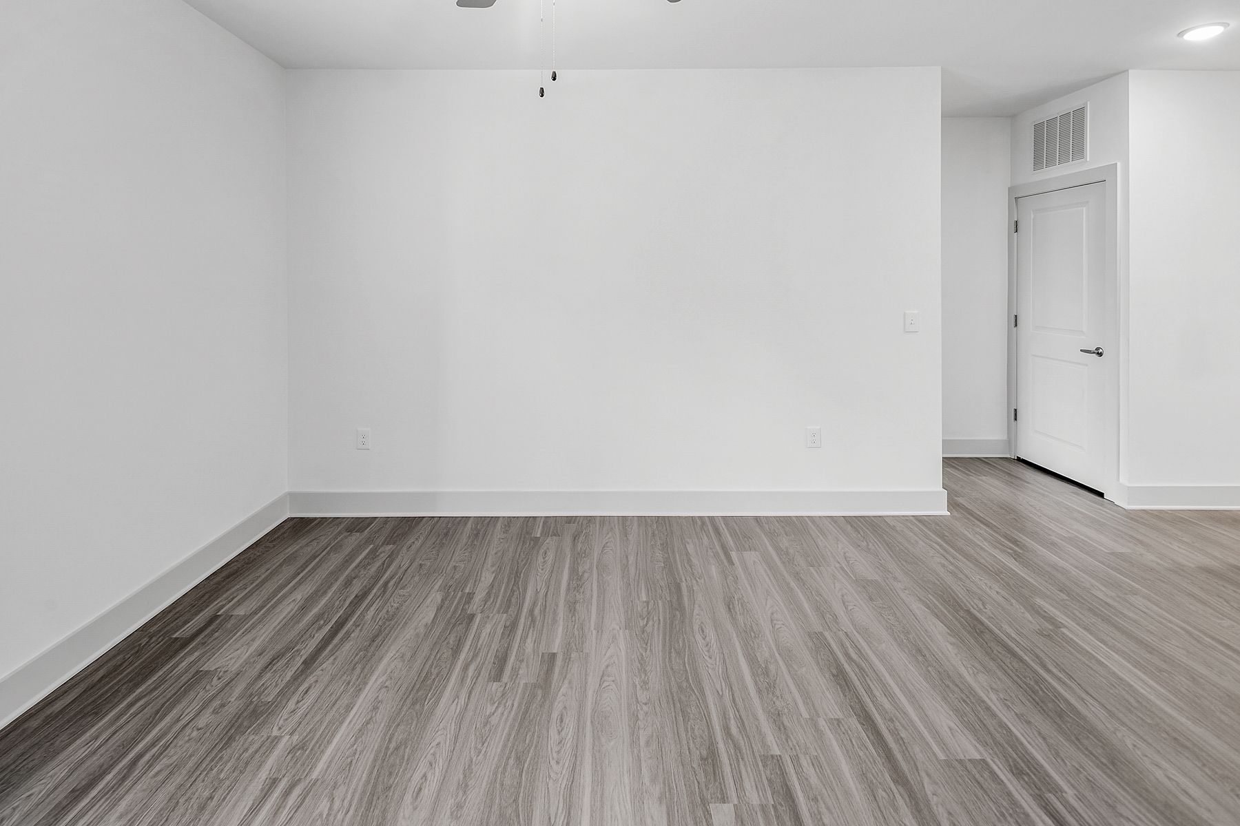 Empty room with white walls, gray wood-look floor, and a door.
