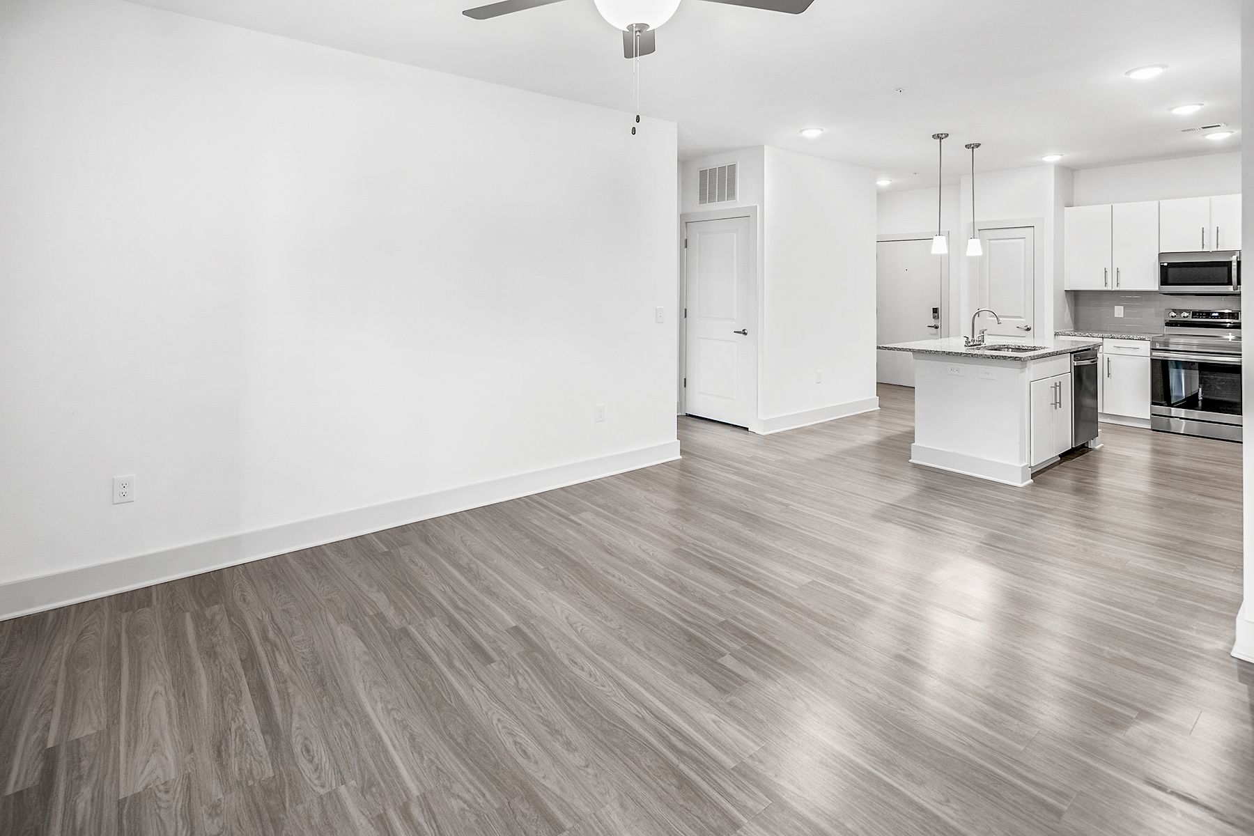 Empty, modern apartment interior with light wood-look floors, white walls, and a kitchen island.