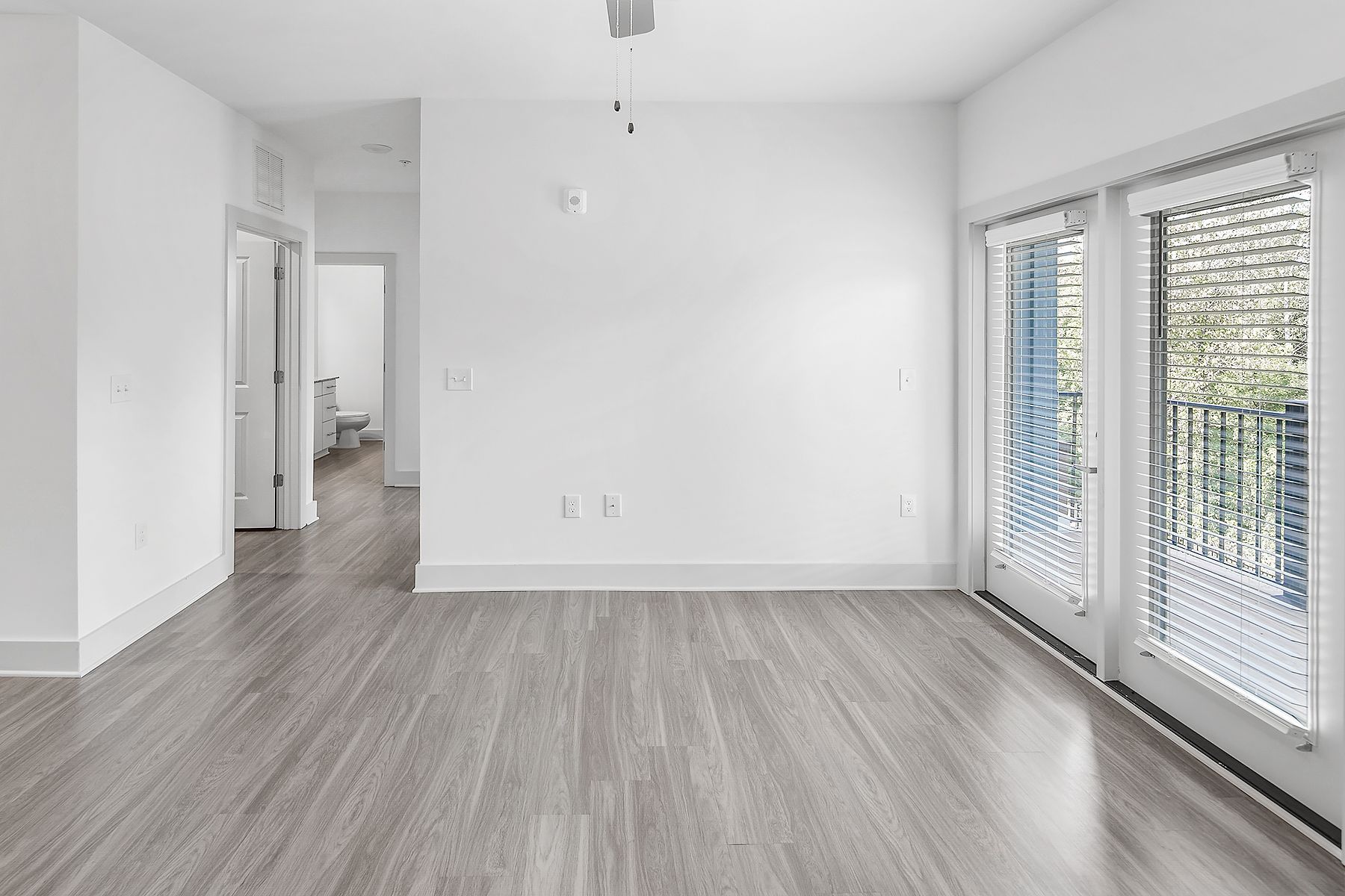 Empty white-walled room with wood-look flooring. French doors on the right, leading to an outdoor space.