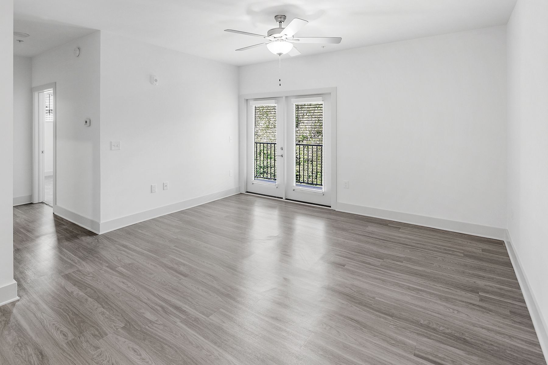 Empty room with gray wood-look flooring, white walls, French doors, and a ceiling fan.