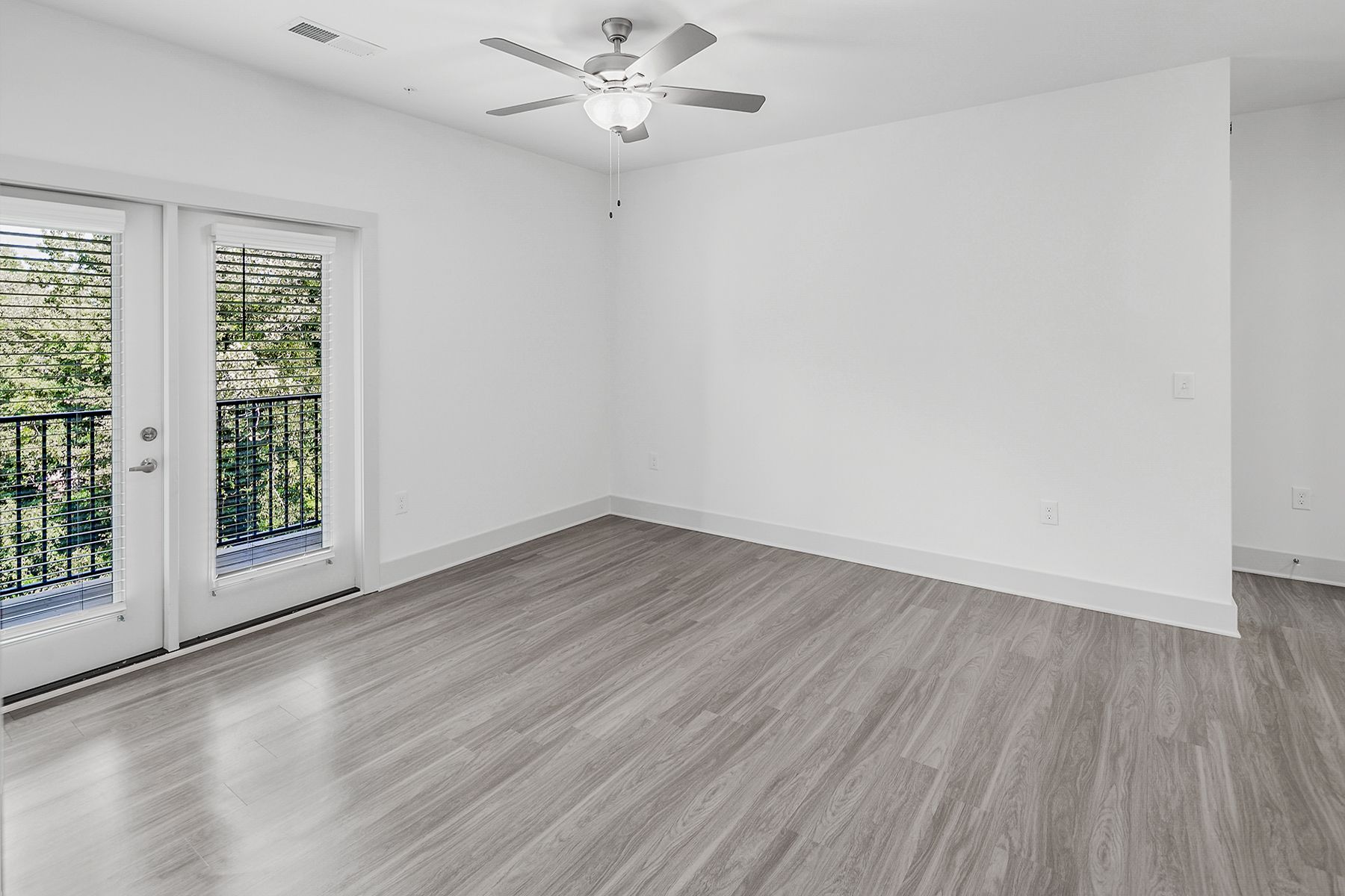 Empty, light-filled room with gray flooring, white walls, and French doors opening to a balcony.