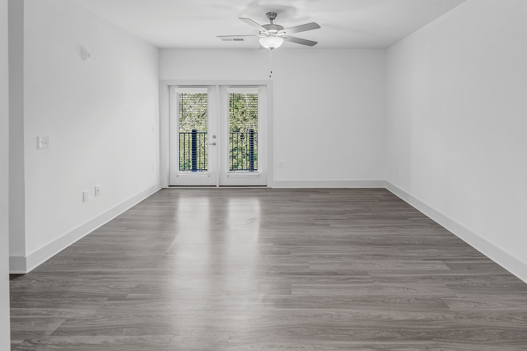 Empty room with white walls, gray wood floor, and French doors to a balcony.