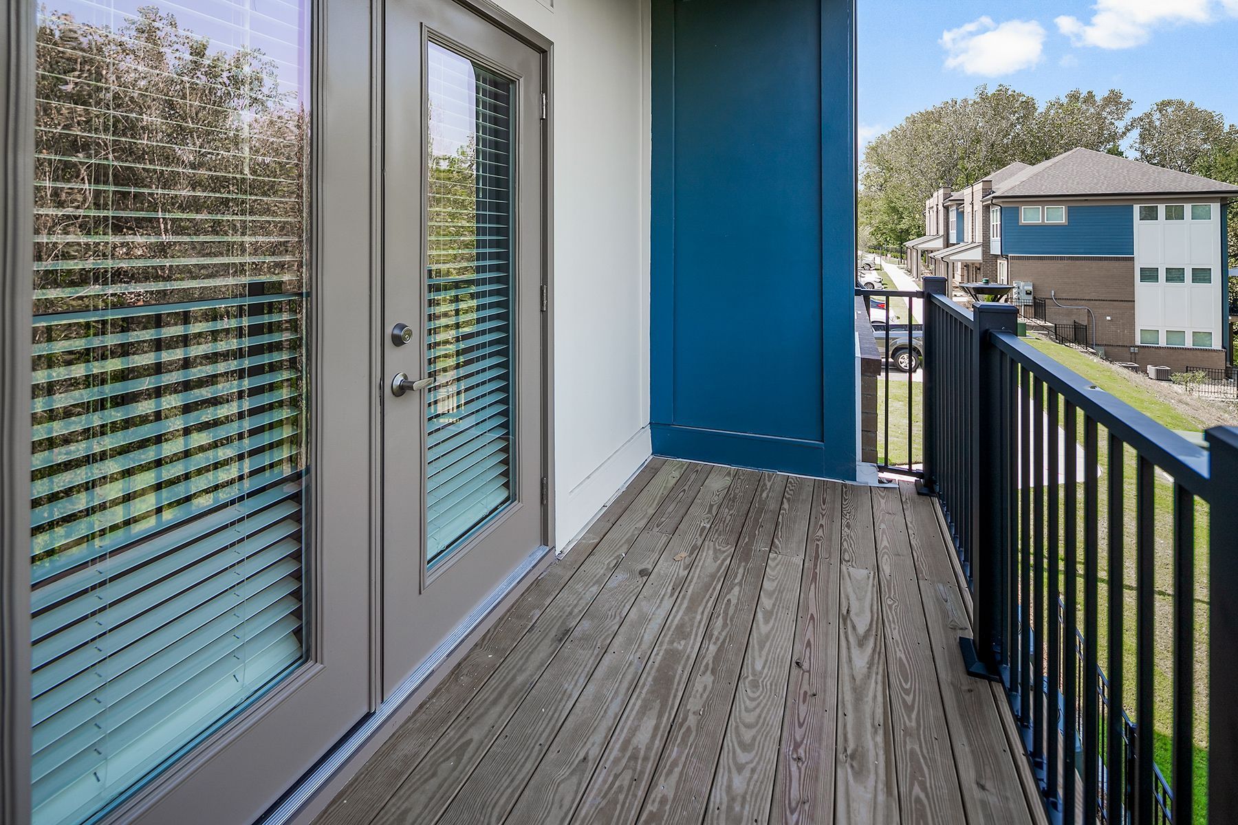 Balcony with French doors, wood flooring, black railing, and blue accent. View of neighboring building.