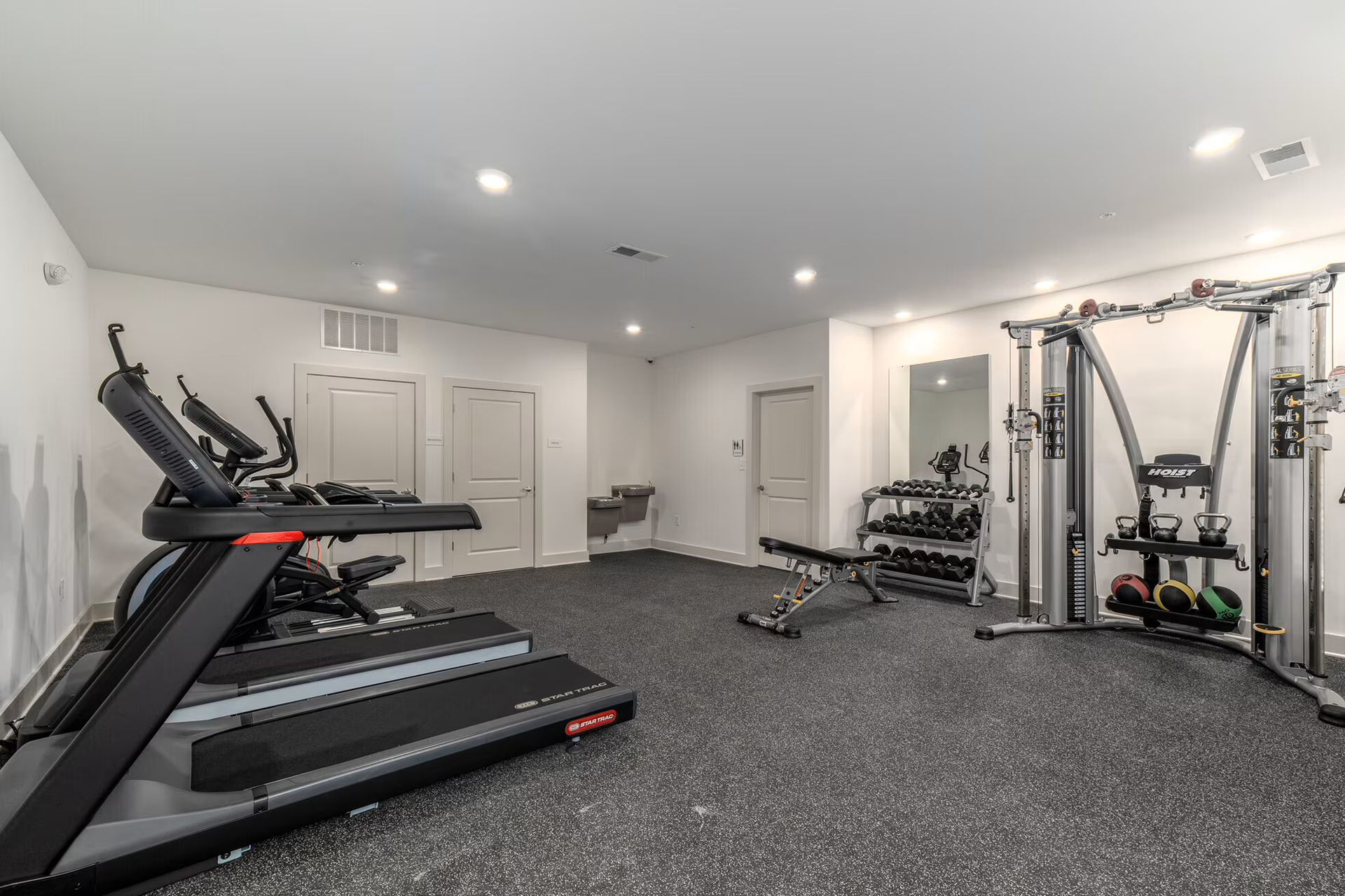 Gym with treadmill, cable machine, free weights, and exercise bench on a dark floor.