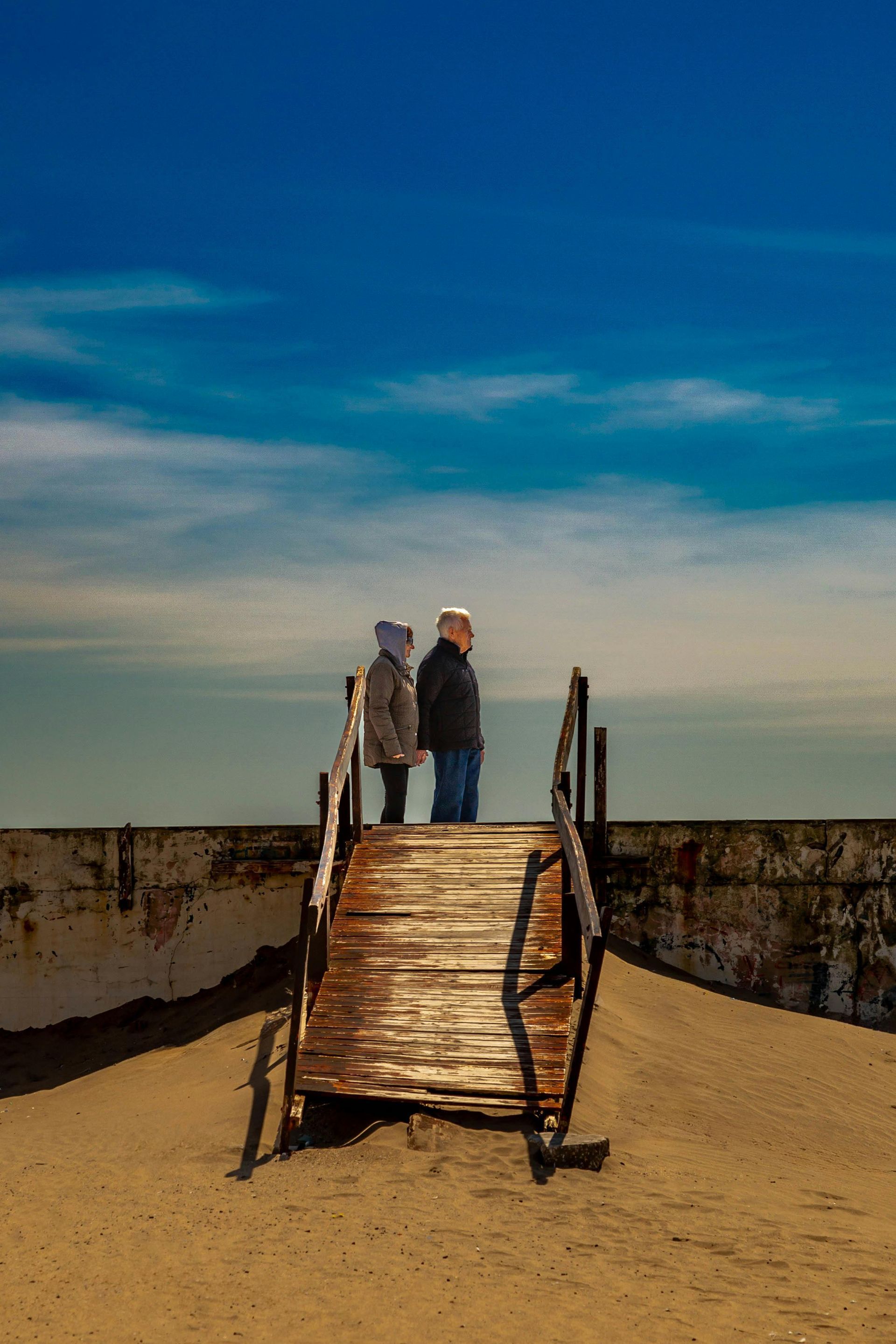 Two people are standing on a wooden bridge over a body of water.