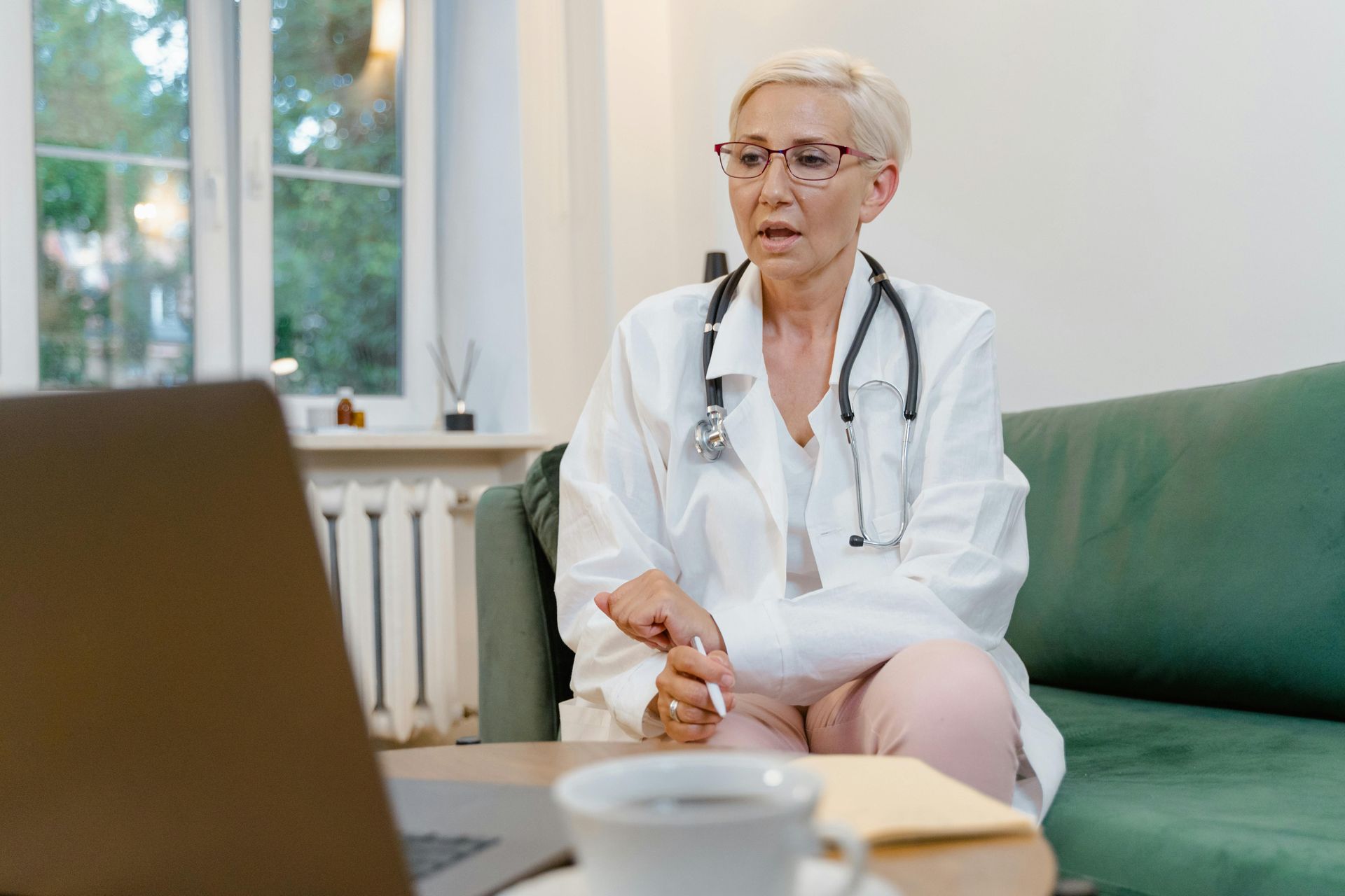 A doctor is sitting on a couch talking to a patient on a video call.