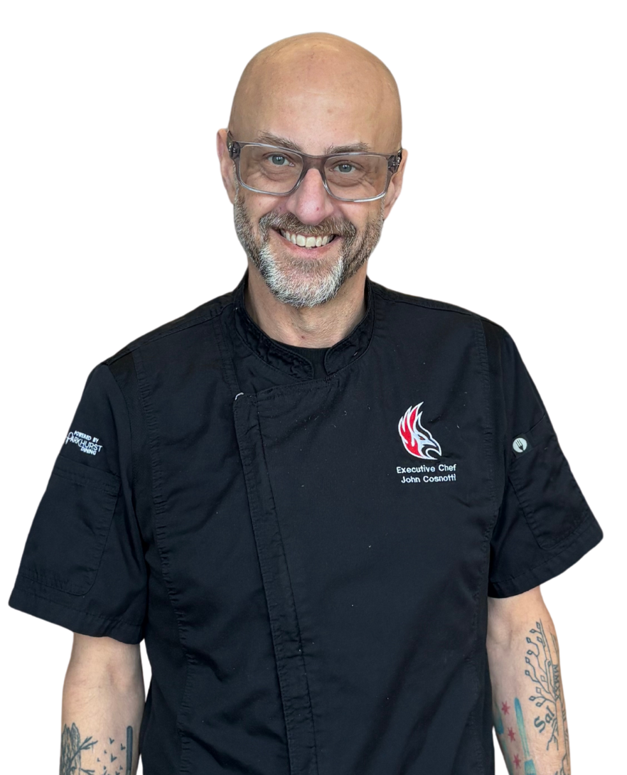 A smiling person wearing glasses and a black chef's coat with a red logo on the chest.