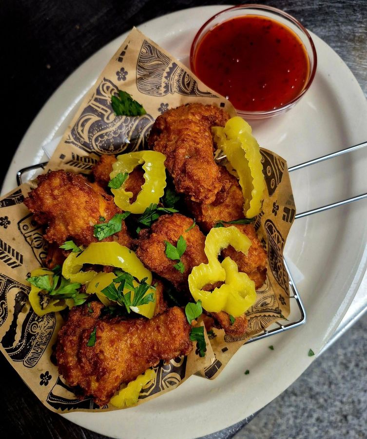 Fried chicken wings with pepper rings and red sauce on a plate.