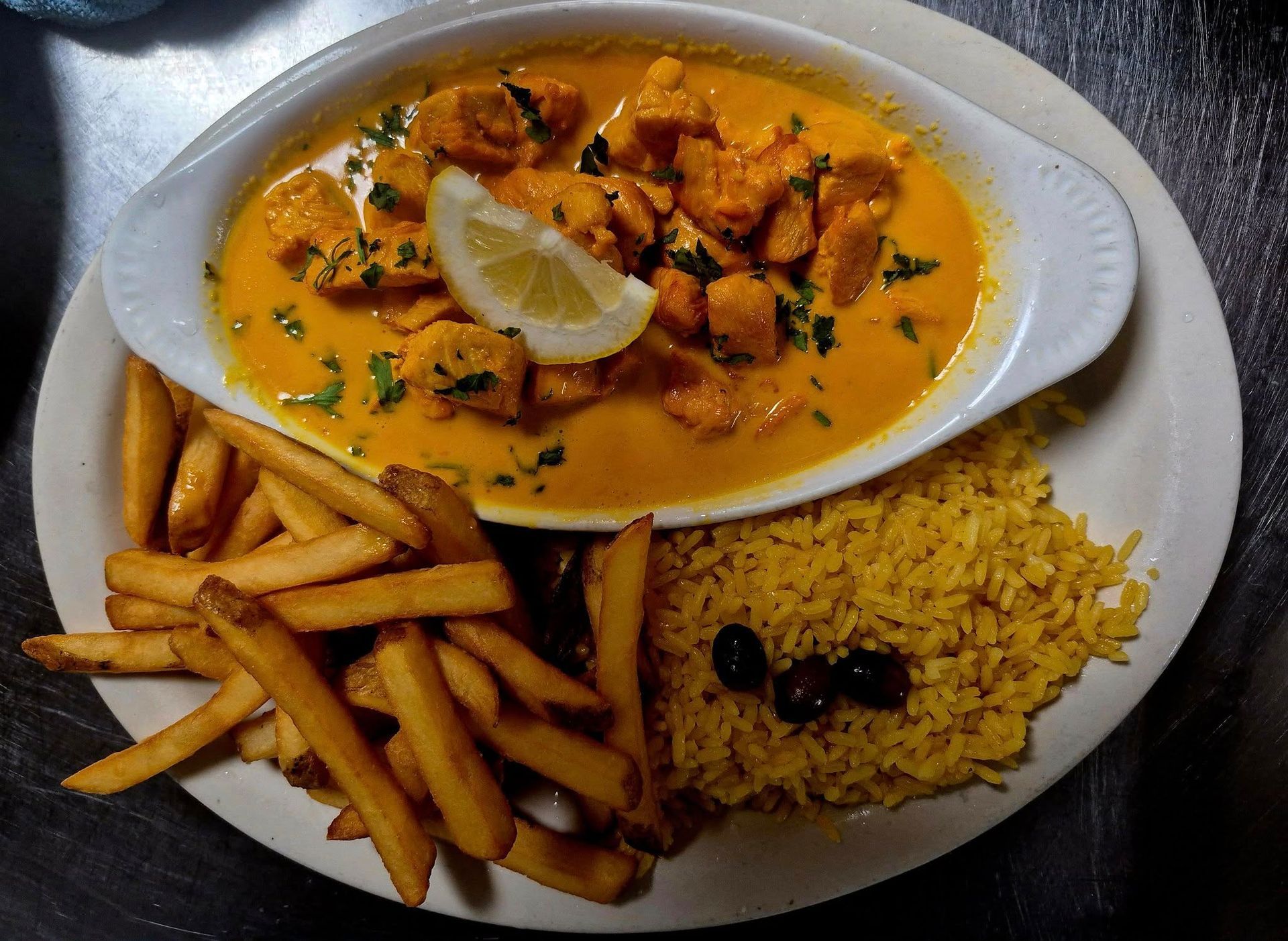 Chicken curry with rice, fries, and lemon garnish on a plate.