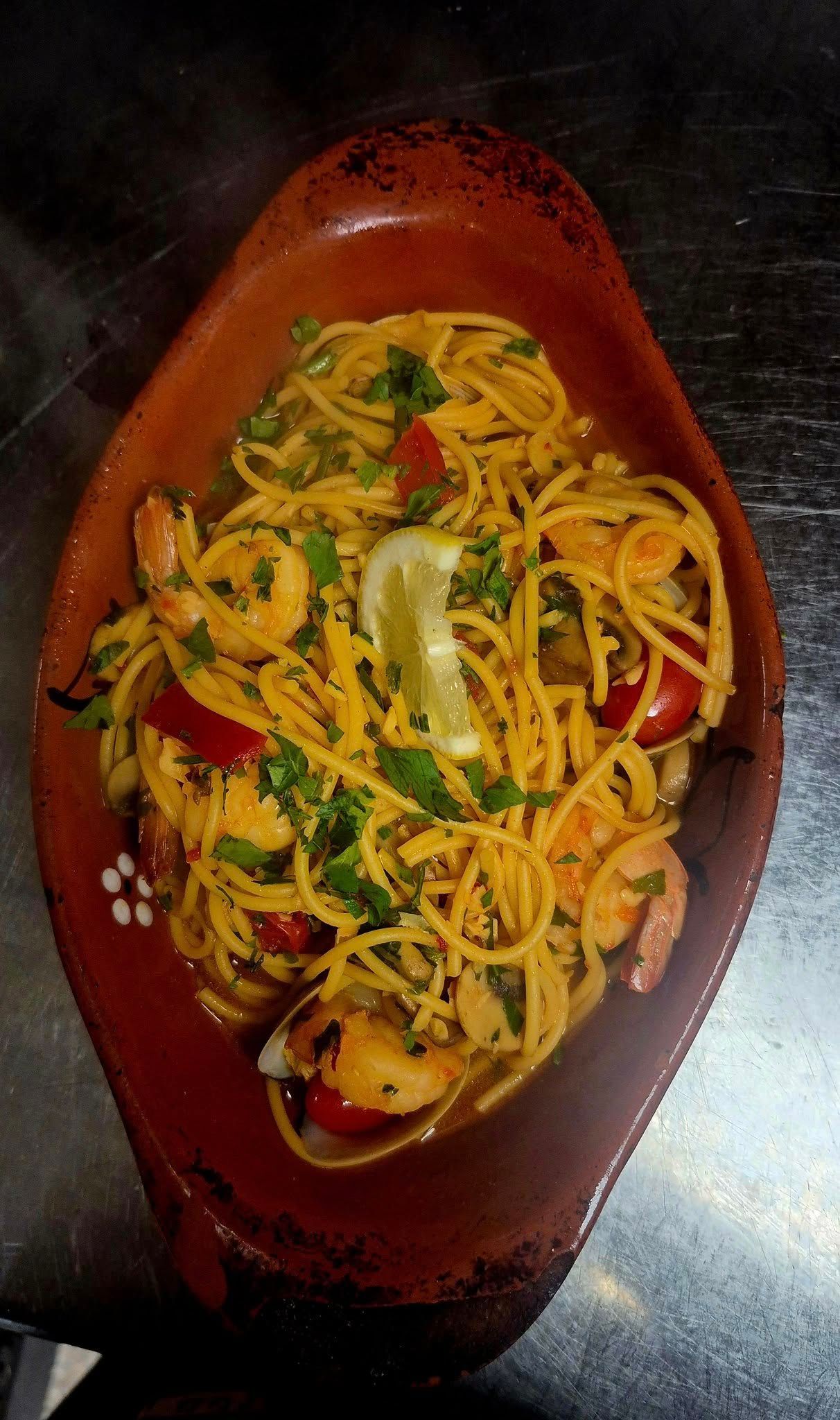Pasta dish with shrimp, tomatoes, and parsley in a brown serving dish, garnished with lemon.