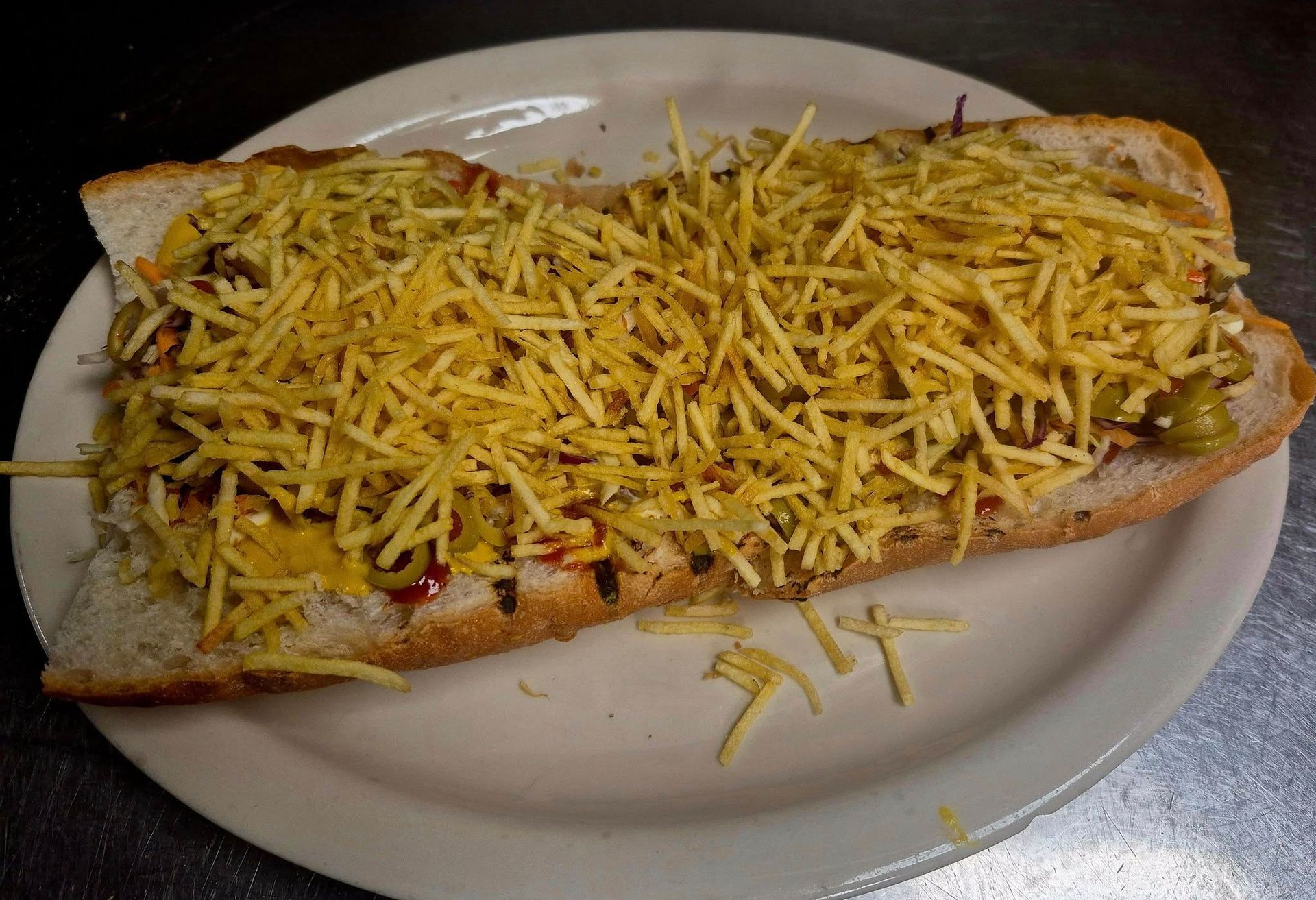 Sub sandwich on a white plate, piled high with shoestring potatoes.