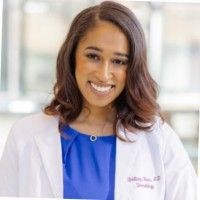 A woman in a lab coat and blue shirt is smiling for the camera.