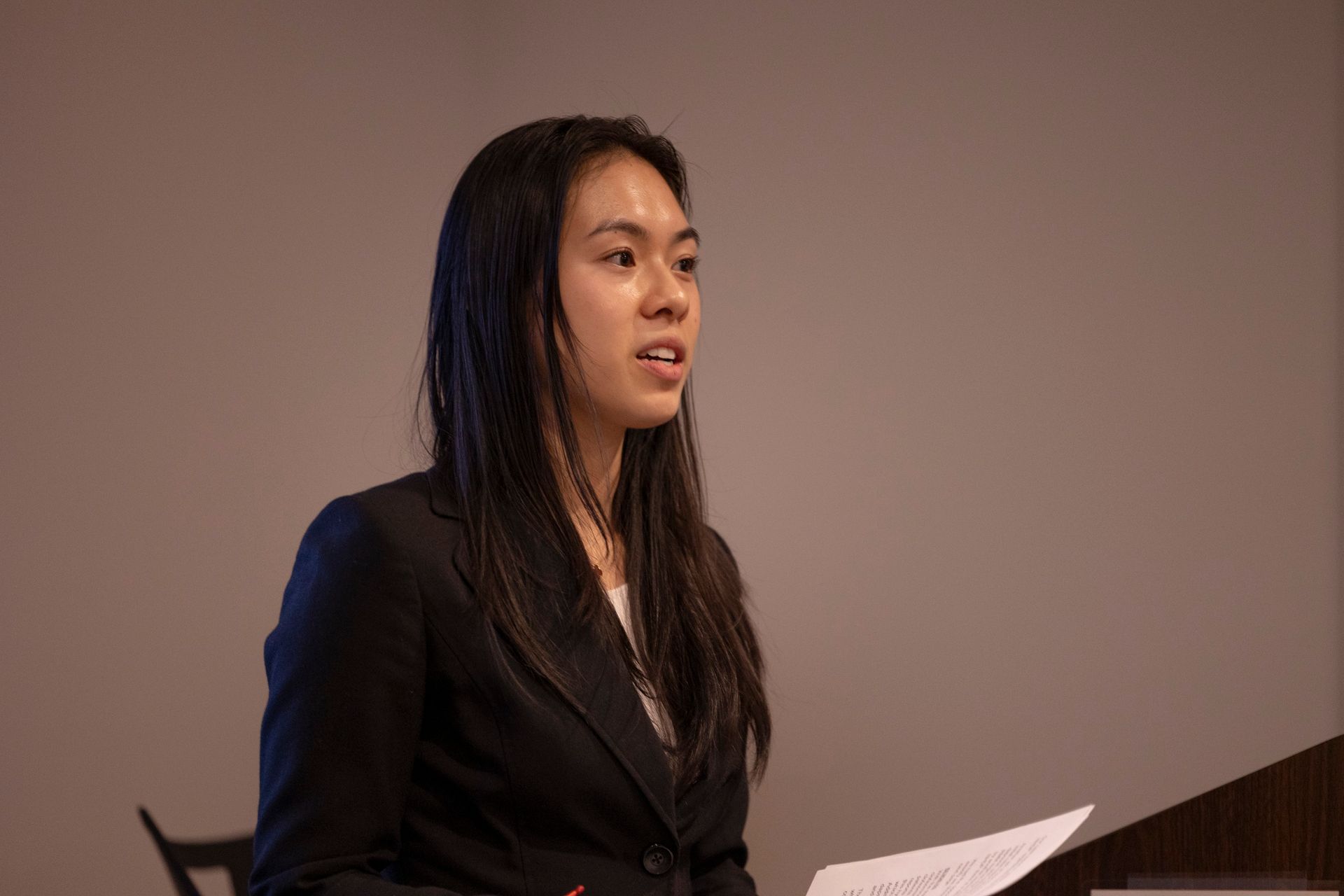 A woman in a suit is giving a speech at a podium.