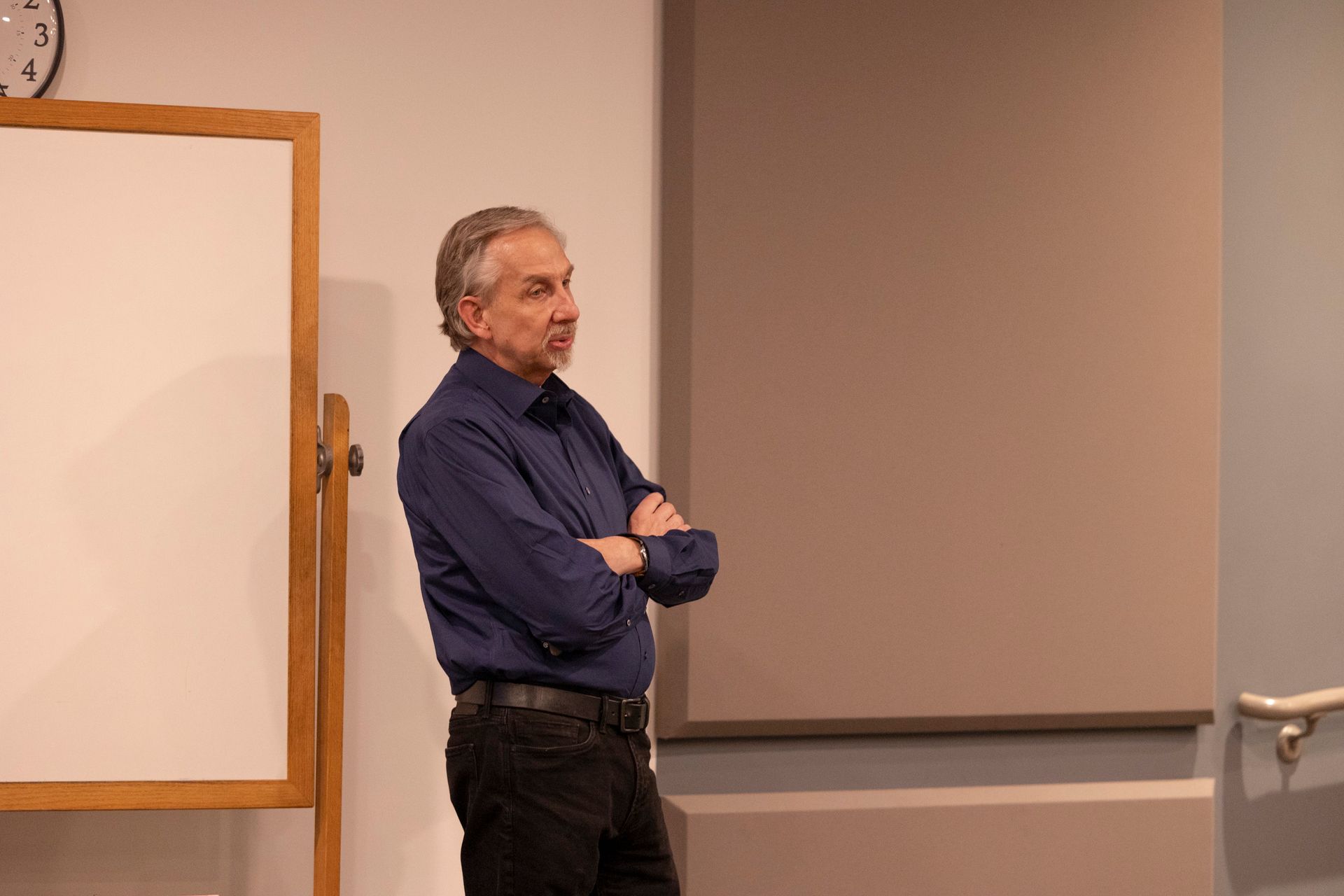 A man in a blue shirt is standing in front of a white board.