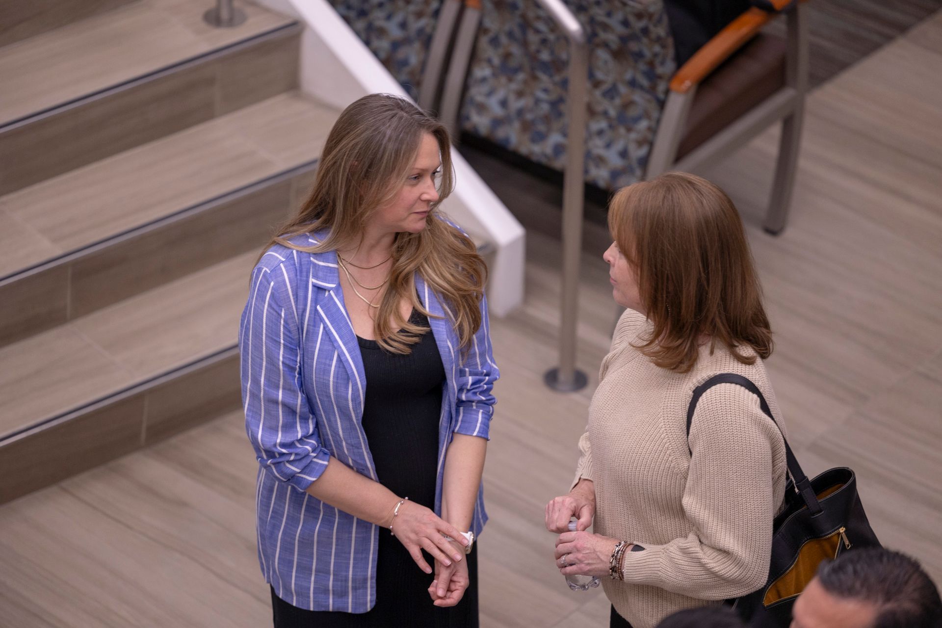 Two women are standing next to each other talking in front of stairs.