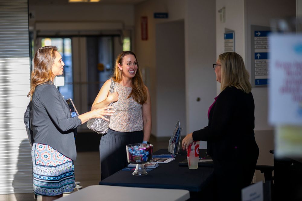 Three women are standing around a table talking to each other.