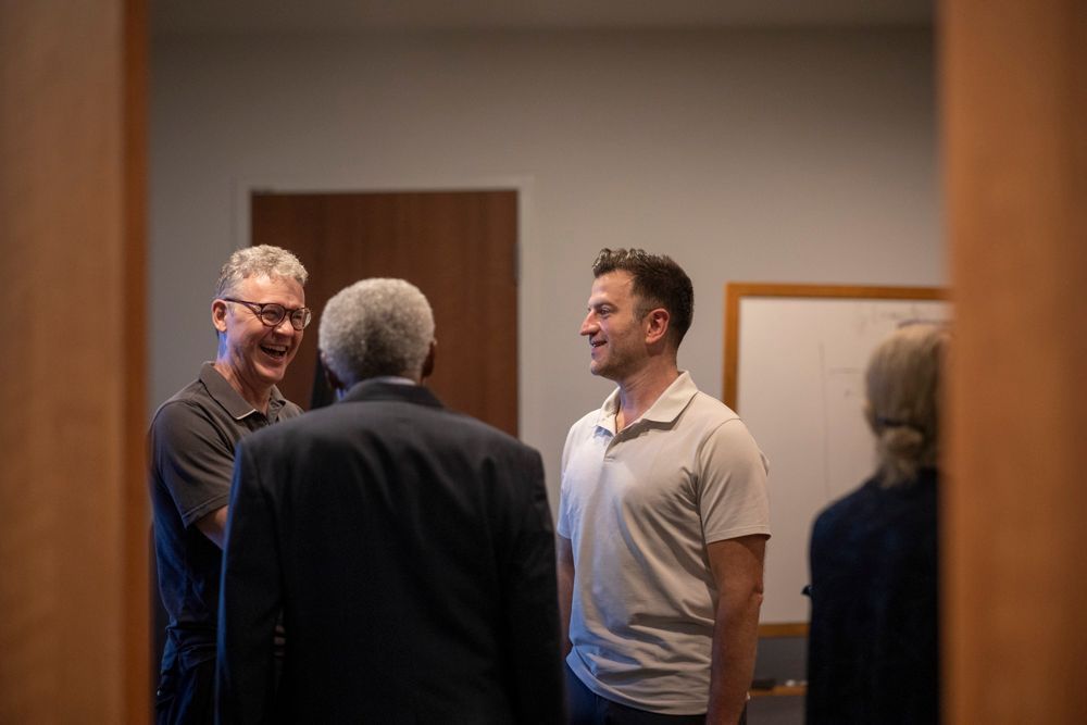 A group of men are standing in a room talking to each other.