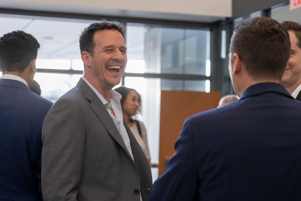 A man in a suit is laughing while talking to another man in a blue suit.