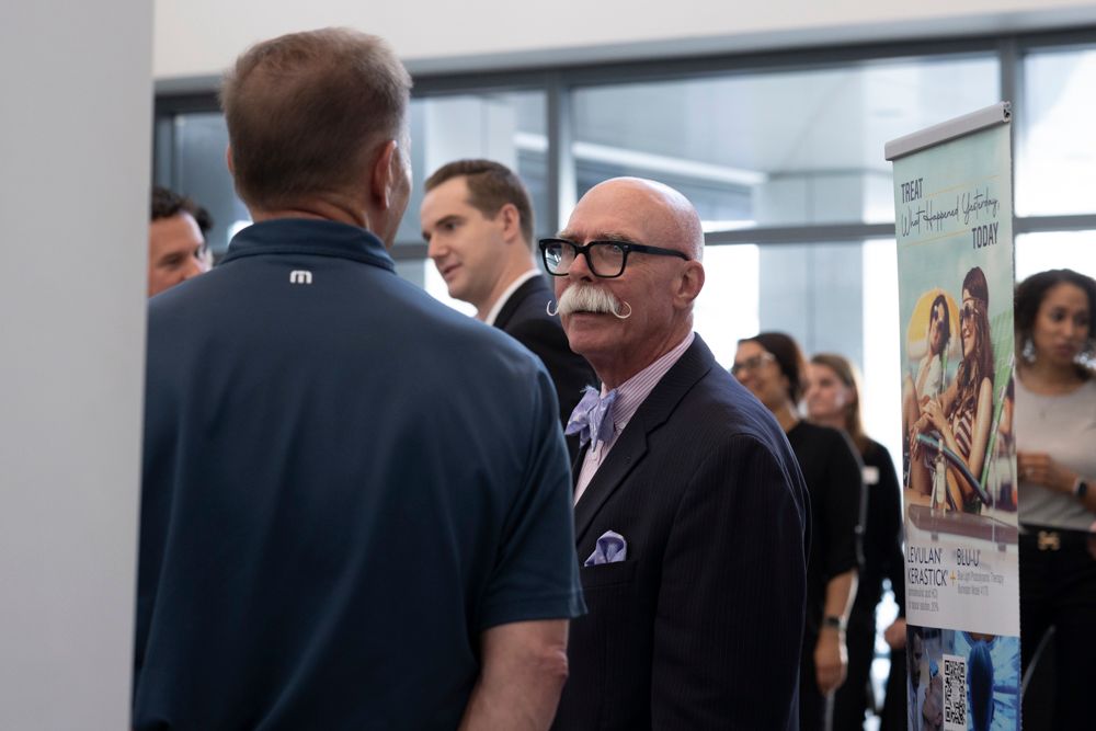 A group of men are standing in a room talking to each other.