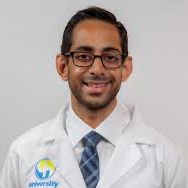A man in a lab coat and tie is smiling for the camera.