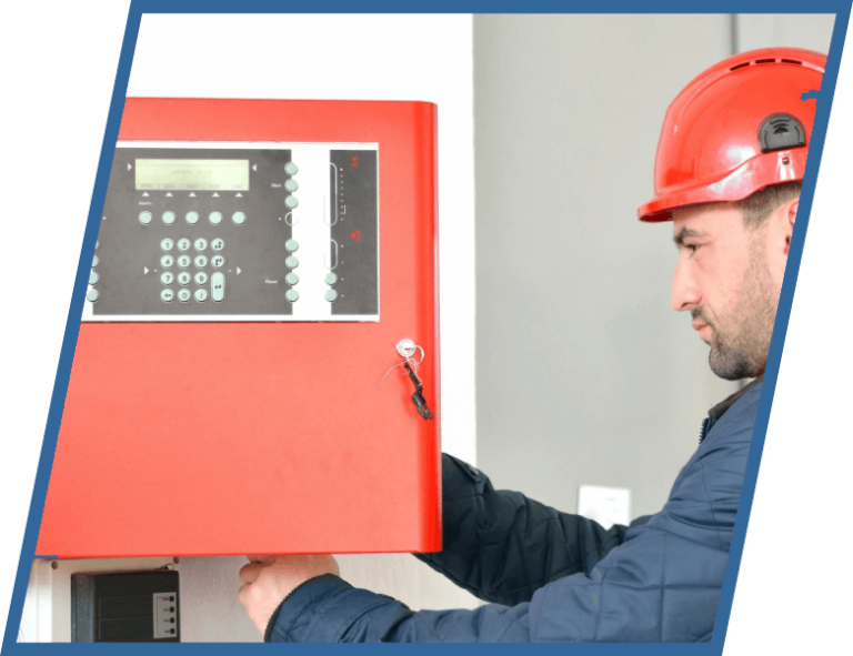 A man wearing a red hard hat is working on a fire alarm system.